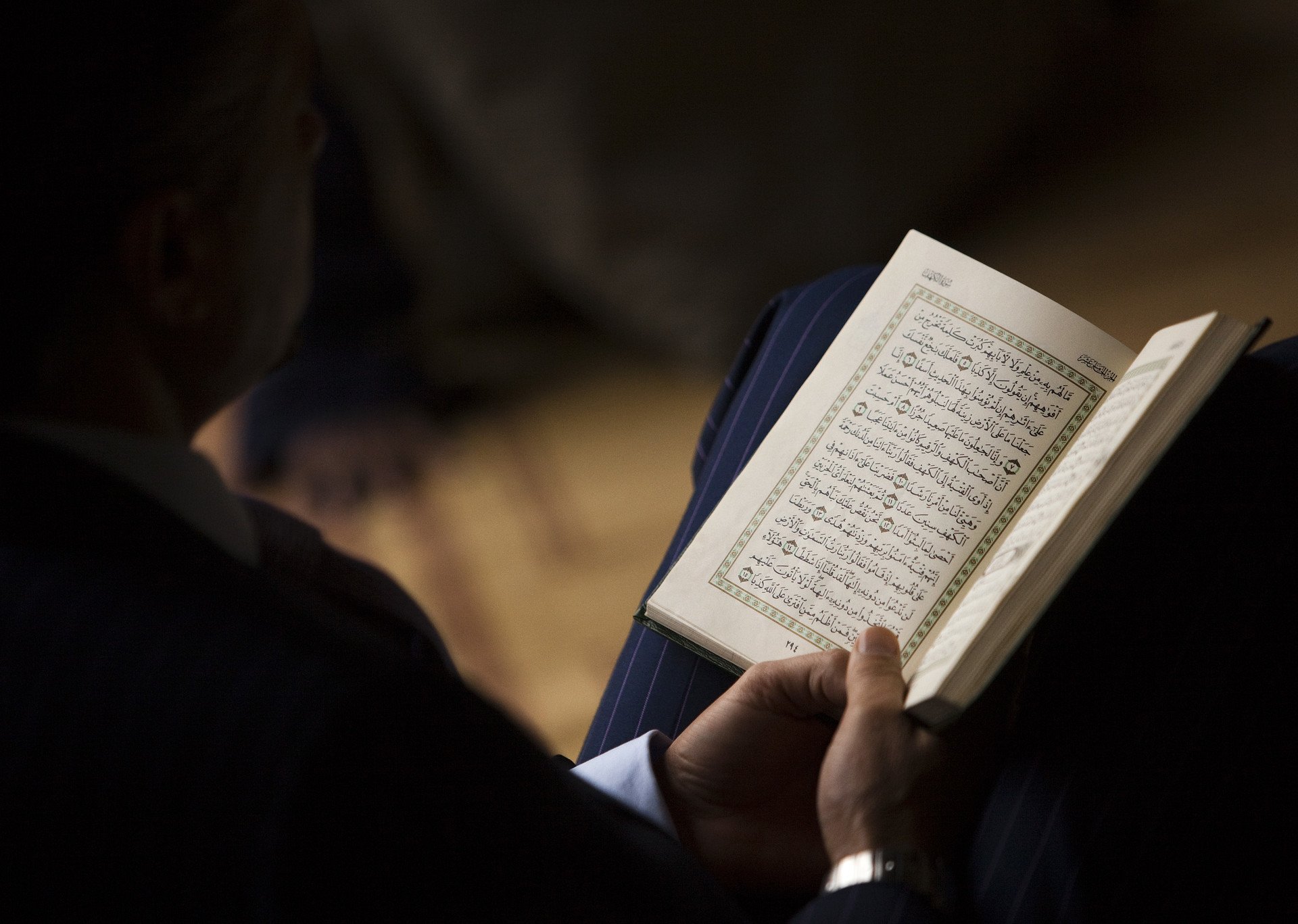 Мусульмански свет. Коран в руках. Чтение Корана. Коран в темноте. Коран в руках человека.