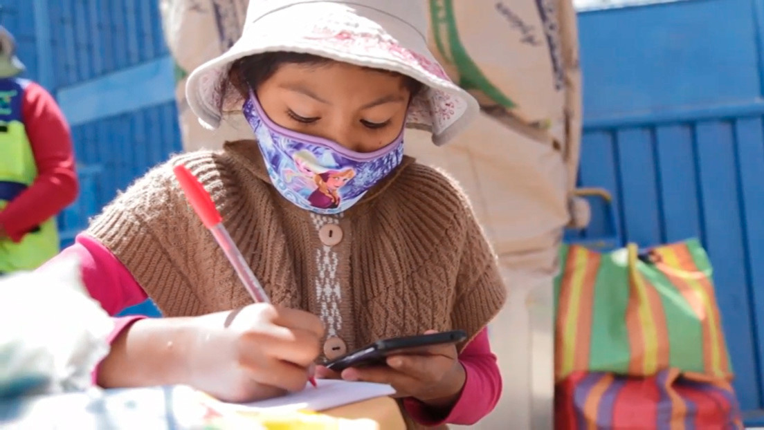 Niña peruana de 10 años estudia a través de un celular, mientras ayuda a su tía en un puesto de venta de refrescos
