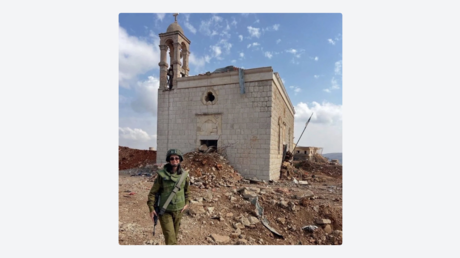 Una soldado israelí posa sonriente ante una iglesia centenaria entre ruinas