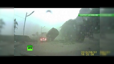 Un auto, a punto de ser aplastado por una enorme roca en una carretera