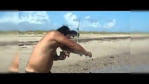 Un hombre agarra un pequeño tiburón y es mordido por él
