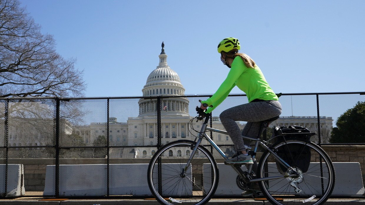 FILE PHOTO: A cyclist looks up at the US Capitol as she rides past security fencing in Washington, DC, March 22, 2021 © Reuters / Kevin Lamarque