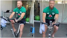 Con the comeback trail: McGregor shows off progress 6 weeks after horror leg break as he pedals on exercise bike (VIDEO)