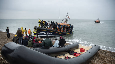 Migrants sit beside a boat used to cross the English Channel in Dungeness, UK, November 24, 2021.