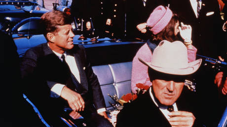 Texas Governor John Connolly adjusts his tie as President and Mrs. Kennedy, in a pink outfit, settled in rear seats, prepared for motorcade into city from airport, Nov. 22. © Bettmann / Getty Images