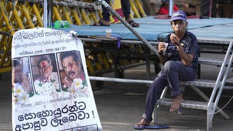 FILE PHOTO: A protester drinks tea as she sits by a defaced poster carrying portraits of ousted president Gotabaya Rajapaksa (C) and his brothers at the entrance to president's office in Colombo, Sri Lanka, July 15, 2022.