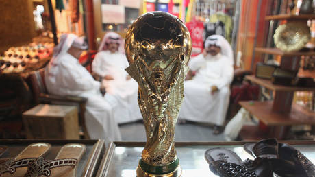 Arab men sit at a shoemaker's stall with a replica of the FIFA World Cup trophy in the Souq Waqif traditional market