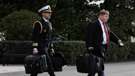 FILE PHOTO of a US military aide (L) carrying a briefcase with the launch codes for nuclear weapons, prior to a departure of President Joe Biden from the White House, Washington, DC, US