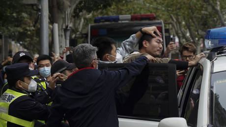 A protester is forced into a police car by the police, during a protest on a street in Shanghai, China, Sunday, Nov. 27, 2022