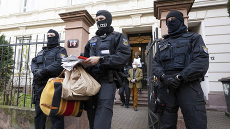 Masked police officers lead Prince Reuss (back, center) to a police vehicle after searching a house in Hessen, Frankfurt/Main during a raid against so-called "Reich citizens",