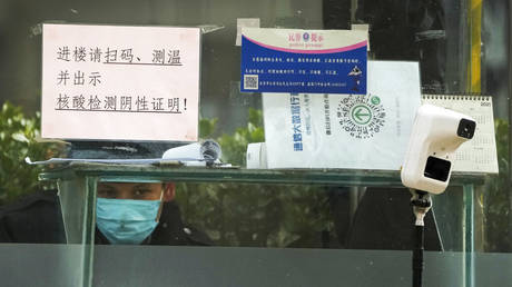 A security guard keeps watch inside a booth displaying a temperature scan device and a travel QR code, outside an office building in Beijing, Monday, Dec. 12, 2022.