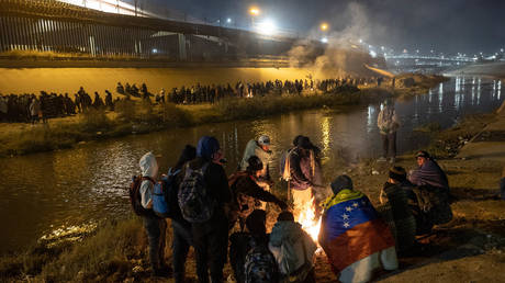Venezuelan immigrants warm by a fire after hundreds of other migrants surged across the Rio Grande into El Paso, Texas to seek asylum on December 19, 2022 as seen from Ciudad Juarez, Mexico.