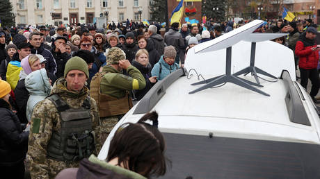 Ukrainians use their mobile phones standing near a Starlink satellite-based broadband station.