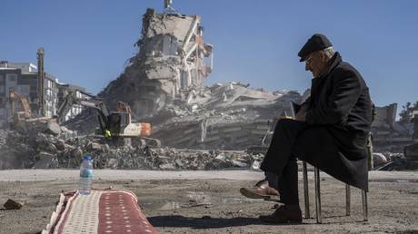 Mehmet Nasir Duran, 67, sits on a chair, as heavy machines remove debris from a building, where five of his family members are trapped in Nurdagi, southeastern Turkey, Thursday, Feb. 9, 2023.