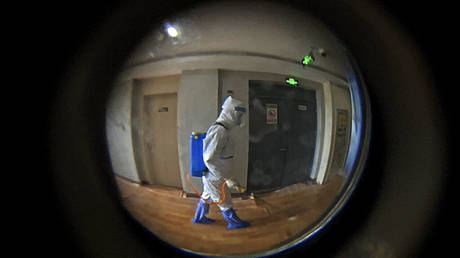 Seen through a peephole in the door, a medical worker wearing protective clothing disinfects the corridor of a hotel used for foreigners to stay during a health quarantine period in Shanghai, China, Thursday, Aug. 12 2021