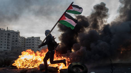 FILE PHOTO: A Palestinian protester runs past a burning barricade carrying a Palestinian flag during clashes with Israeli border guards near an Israeli checkpoint.