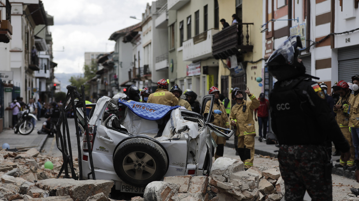 A police officer looks up next to a car crushed by debris after an earthquake shook Cuenca, Ecuador, March 18, 2023