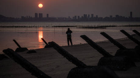 A man takes photographs of the sunset over Chinese city Xiamen amid anti-tank fortifications from previous conflicts on April 09, 2023 in Kinmen, Taiwan