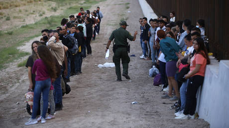 FILE PHOTO: A group of migrants stand next to the border wall as a US Border Patrol agent takes a head count in Eagle Pass, Texas, May 21, 2022.