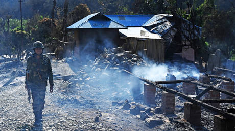 An Indian army soldier walks past the remains of a house that was set on fire by a mob in the ethnic violence hit area of Heiroklian village in Senapati district, in India's Manipur state on May 8, 2023.