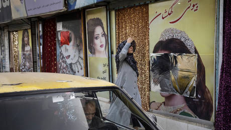 FILE PHOTO: A woman walks past beauty salons with window decorations which have been defaced in Kabul, Afghanistan, September 12, 2021