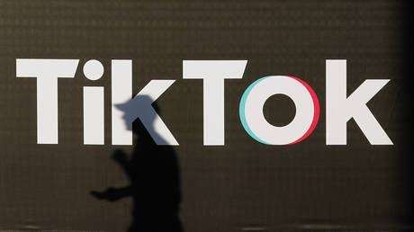 A young man holding a smartphone casts a shadow as he walks past an advertisement for social media company TikTok on September 21, 2020 in Berlin, Germany