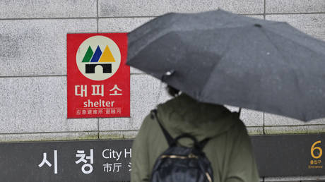 A woman holding an umbrella walks past a shelter sign set up on an exit of a subway station during a civil defence drill against possible artillery attacks by North Korea in Seoul on August 23, 2023.