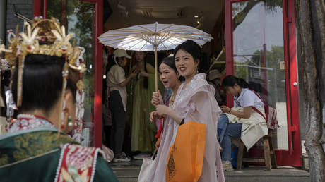 Women dressed in traditional costumes walk by vendors near the Forbidden City in Beijing, China, May 2, 2023