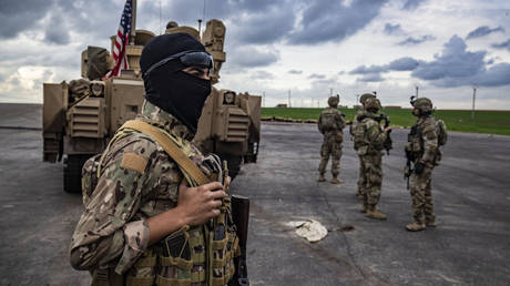 A member of the Syrian Democratic Forces (SDF) and US soldiers stand near an armored military vehicle in Syria's northeastern Hasakeh province.