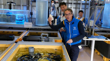 Rafael Mariano Grossi, Director General of the International Atomic Energy Agency, shows off an empty bottle after he fed flounder in a fish tank filled with treated wastewater at a lab, while visiting the damaged Fukushima nuclear power plant on July 5, 2023 in Fukushima, Japan.