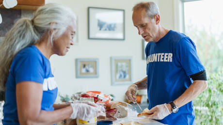 A retired mature adult man works with his wife as a volunteer preparing meals for those in need.