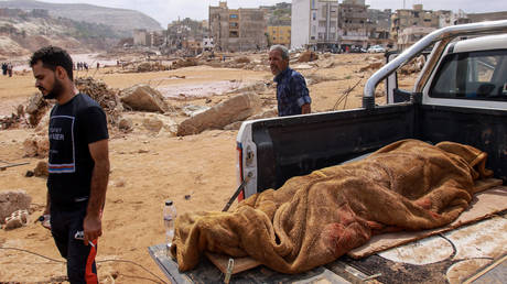 People walk past the body of a flash flood victim in Derna, eastern Libya, on September 11, 2023