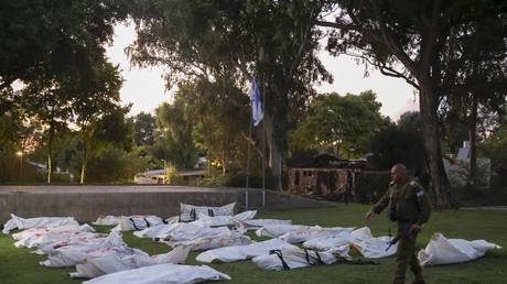 A member of Israeli security walks past covered bodies at kibbutz Beeri near the border with Gaza, October 11, 2023