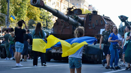 A girl with a Ukrainian flag runs past a destroyed armored vehicle, said to be Russian, put on display in central Kiev, Ukraine.