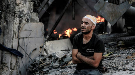 An injured man sits in front of a smoldering building in the aftermath of an Israeli strike on Gaza City on October 26, 2023