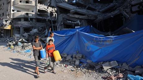 Palestinian boys carry containers as they walk past destroyed buildings in the Nuseirat refugee camp, Gaza, October 30, 2023