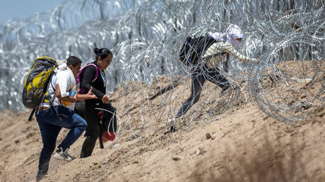 Migrants try to get through razor wire surrounding a makeshift camp after crossing the border near El Paso, Texas, in May.