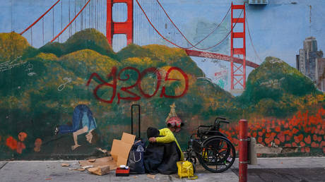 A homeless person lies against a mural of the Golden Gate Bridge near APEC Summit headquarters on November 11, 2023 in downtown San Francisco, California