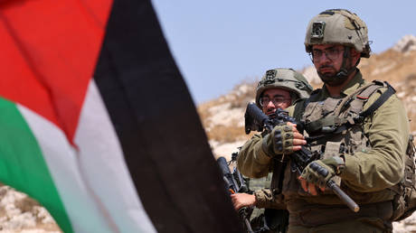 Israeli soldiers stand behind a Palestinian flag held by a protester during a demonstration against the confiscation of lands on the outskirts of the village of Beit Dajan east of the occupied-West Bank city of Nablus on August 18, 2023.