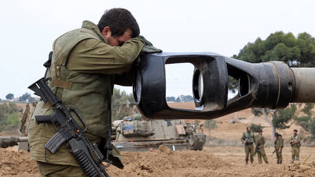 An Israeli soldier rests his head on the gun barrel of a self-propelled artillery howitzer as Israeli soldiers take positions near the border with Gaza in southern Israel on October 9, 2023.