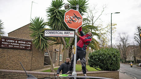 A person removes a piece of art work by Banksy at the intersection of Southampton Way and Commercial Way in Peckham, south east London, December 22, 2023