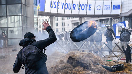 Protester throws a burning tyre in front of police forces during the farmer protest action in the European district in Brussels, Belgium.
