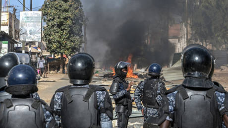 Senegalese police officers stand in formation on a road blocked with burning barricades during demonstrations called by the opposition parties in Dakar on February 4, 2024.
