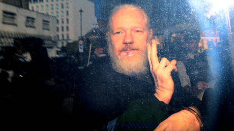 Julian Assange gestures to the media from a police vehicle on his arrival at Westminster Magistrates court on April 11, 2019 in London, England