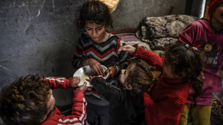 Children displaced by the Israel-Hamas war try to eat from a single bowl on Wednesday in Rafah, Gaza.
