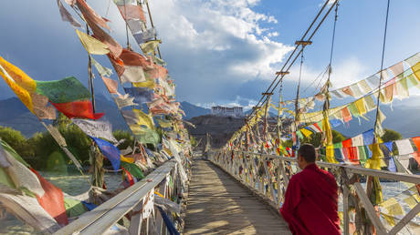 Buddhist monk crossing bridge covered in prayer flags, Stakna monastery, nr Leh, Ladakh, India.