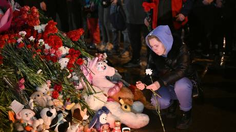 A woman lights a candle at a makeshift memorial near the Crocus City Hall in memory of the victims of a terrorist attack on the concert venue near Moscow on March 22, Russia.