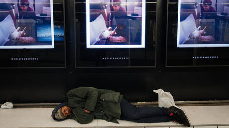 A homeless man sleeps under advertising screens at Concorde metro station on March 25, 2024