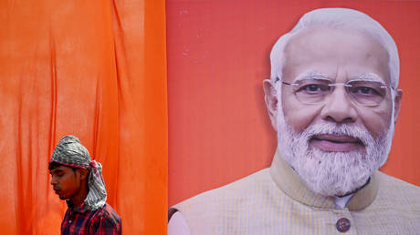 A worker walks past a hoarding of India's Prime Minister Narendra Modi, leader of the ruling BJP in Raipur on April 15, 2024.