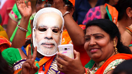 Indian supporters of the Bhartiya Janta Party (BJP), with one wearing a mask of Prime Minister Narendra Modi, take a selfie as they take part in an election rally in Chittorgarh, in the western state of Rajasthan, on April 21, 2019.